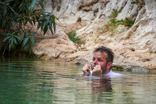 Portrait of tourist, man with hands out of water and shirt in water up to neck. Rock is in Background, Oman.
