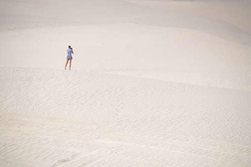 Back view of a woman  standing and  photographing morning at White dunes, called Sugar dunes at Al Khaluf, Oman. It is south part of Wahiba desert, near Arabian sea.