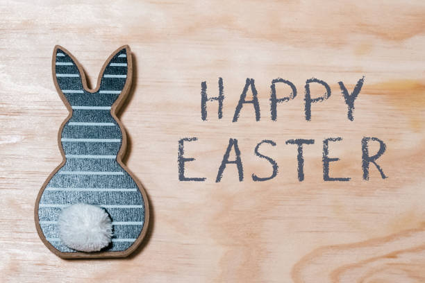A rabbit with a white fluffy tail is on a wooden surface. The rabbit is surrounded by a blue and white striped background. The background is decorated with a happy Easter message