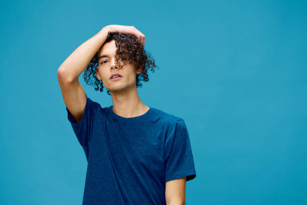 istock Handsome serious curly tanned Caucasian guy in basic t-shirt touches head posing isolated on over blue background. Lifestyle and Emotions concept. Good offer with copy space for ad 2147623038