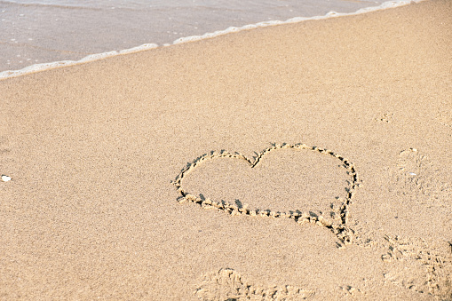 heart engraved in the sand on the shore of a beach, summer love concept