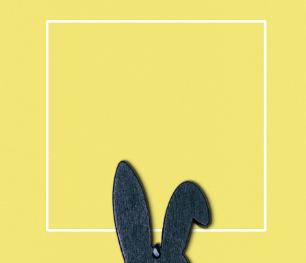 A black rabbit is peeking out from behind a yellow background. The rabbit is the main focus of the image, and the yellow background serves as a neutral and bright contrast to the black rabbit