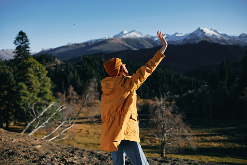 Woman full-length hiker standing with her back raised hands up on the mountain of happiness in yellow raincoat travel autumn and hiking in the mountains in the sunset freedom. High quality photo