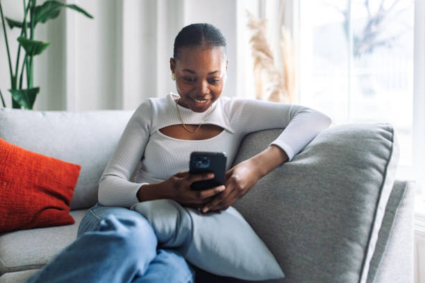 istock Young black woman enjoying smartphone on couch 2147633641