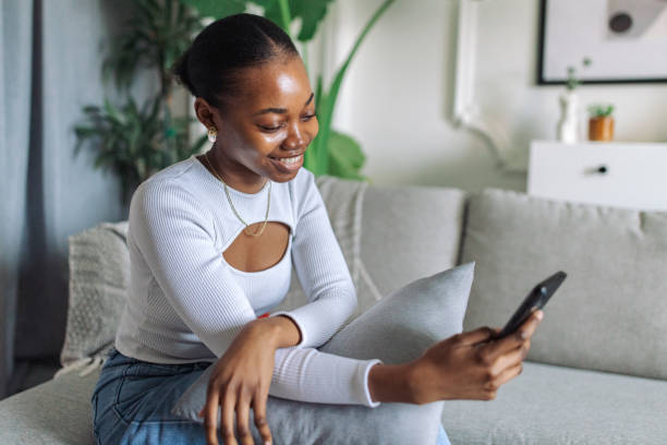 istock Smiling black woman relaxing with smartphone at home 2147634408