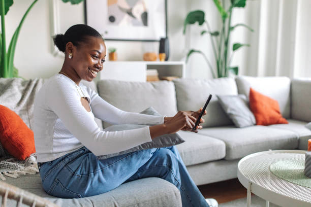 istock Smiling black woman using smartphone in cozy living room 2147634580