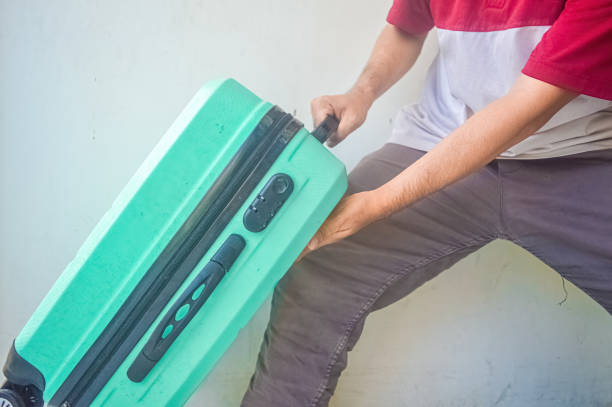 istock man holding a turquoise green suitcase that almost fell 2147635499
