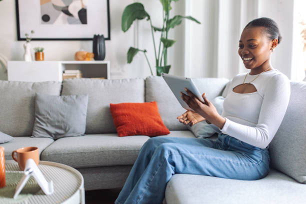 istock Smiling black woman relaxing with tablet on sofa 2147635713