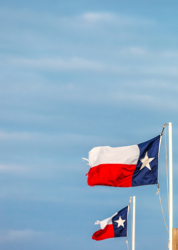 Texas State flags on the pole waving in the wing against blue sky. Port Isabel, Texas, USA