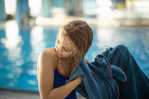 Young girl drying hair with towel after swimming indoors.