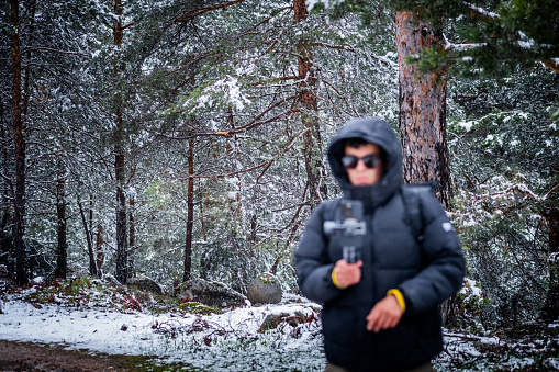 Blurred photo of an adult wearing black coat, hood, and sunglasses, using a gimbal record landscape
