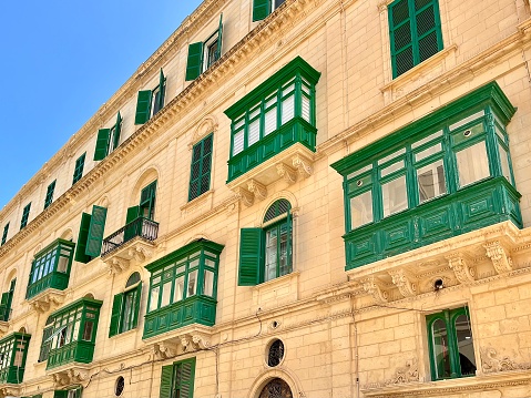 view of an old stone building with traditional green wooden balconies in valletta malta on a sunny summer day