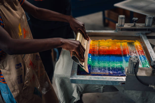 istock Close up of interracial worker's hands with squeegee silkscreen printing 2147648534
