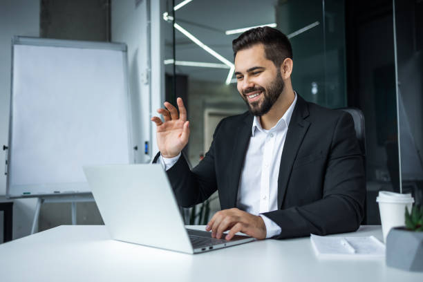 istock Young bearded business man talking, greeting, teleworking, having virtual meeting working on laptop computer giving online training on video conference call. 2147648728