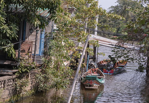 Bangkok, Thailand - Dec 21, 2019 - One wooden rowboat and Two small motor boat moored behind house on canal amongst trees and water. Space for text, Selective focus.