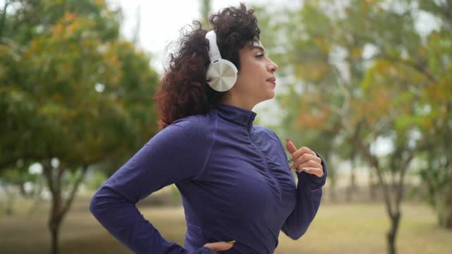 Young woman listen music on headphone and running through the public park