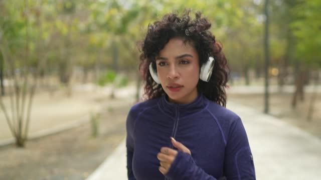 Young woman listen music on headphone and running through the public park