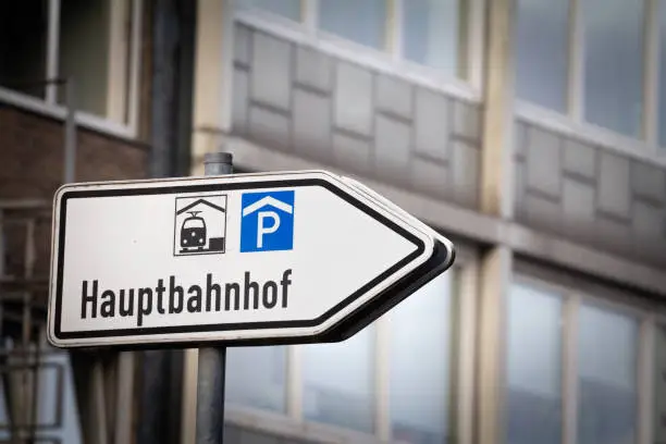 Captured in the image is a directional sign for Aachen Hauptbahnhof, situated in Germany. This sign, marked prominently in black and white, features a train symbol and a parking icon, efficiently guiding travelers to the central railway station and nearby parking facilities. Aachen Hauptbahnhof serves as a pivotal nexus for regional and long-distance travel, emphasizing Germany's commitment to seamless, integrated modes of transportation. The sign represents the essential information needed for smooth transit in a bustling urban environment, highlighting the structured and organized nature of transportation systems in German cities.