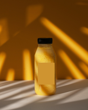 Fruity yellow smoothie in a plastic bottle. Golden-hued smoothie in a bottle, with dramatic shadows, evoking warmth and health. Detox