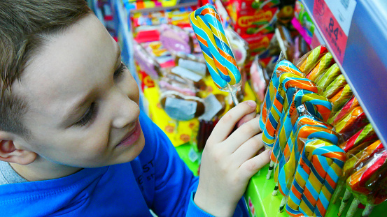 A boy takes a colorful lollipop in a supermarket