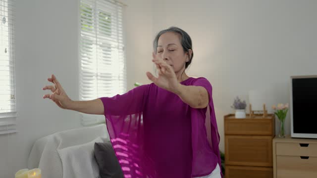 an old woman is doing yoga in the living room in the morning which is her daily routine for health and flexibility of the body, a retired woman is doing light exercise to strengthen her body.