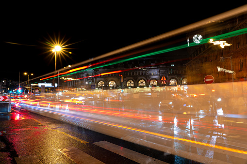 Low exposure photo of car lights passing in front of the facade of the Gare de Lyon train station. Paris. France. August 11, 2023.