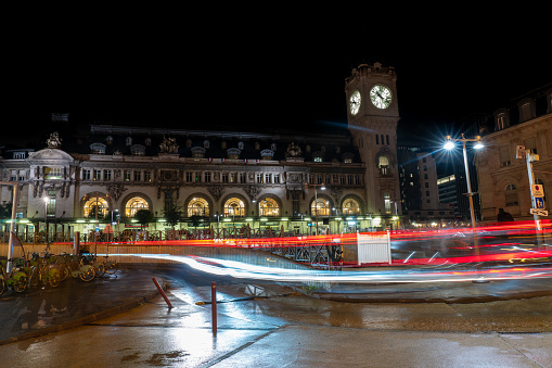 Low exposure photo of the facade of the Gare de Lyon train station with the lights of cars passing in front of them. Paris. France. August 11, 2023.