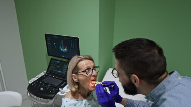 Doctor looking in patient’s mouth using a tongue depressor.
