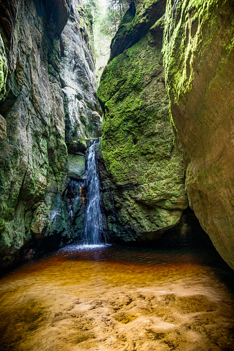 A small waterfall cascades down the rocky walls of the Adrspach Teplice canyon in Czech Republic. The water flows gently, creating a soothing sound and adding to the natural beauty of the canyon.