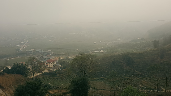 A foggy rural landscape with terraced fields and a singular house
