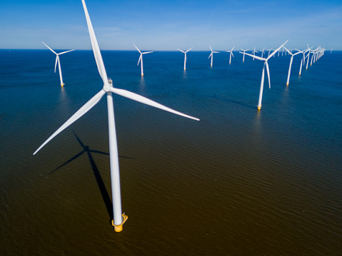 A group of majestic wind turbines standing tall in the ocean against a cloudy sky, harnessing the power of the wind to generate sustainable energy. drone aerial view of windmill turbines