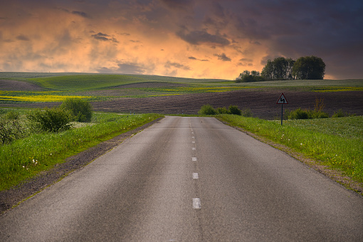 Empty two lane asphalt road running through a serene and open countryside landscape. Surrounding the road are grassy plains and small hills