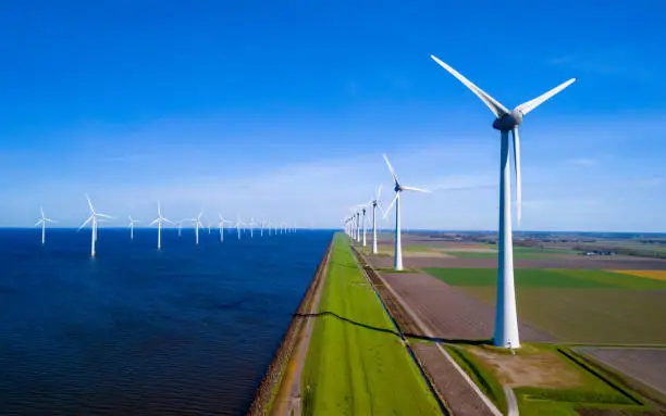 A striking line of wind turbines in the beautiful landscape of the Netherlands Flevoland during the fresh Spring season. green energy, energy transition, windmill turbines on land and in ocean