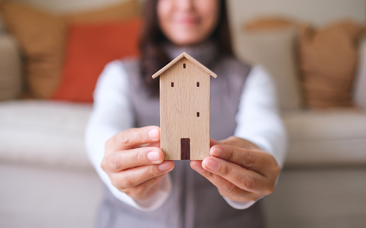 Closeup image of a young woman holding and showing a wooden house model