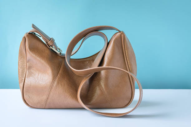 Brown colour leather woman handbag on white table. Blue background.