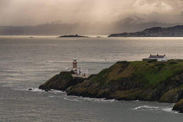 Photo of Howth Cliffs, Dublin, Ireland. Cloudy landscape with Ireland coastline, Howth Lighthouse and North Sea. Howth Cliffs Walk.