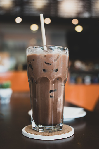 Chocolate milk drink glass with paper straw and bokeh light background