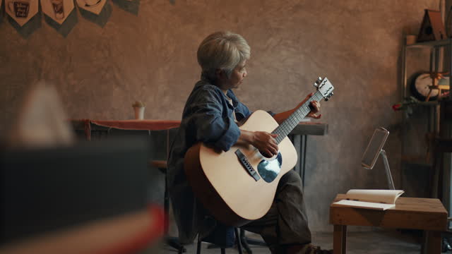 Senior woman plays guitar music as a hobby at home.
