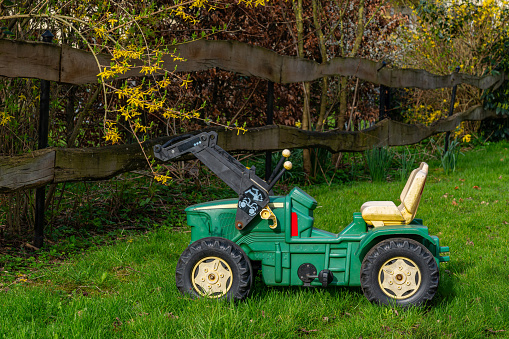 Plastic toy children's tractor on a green lawn near a wooden fence. Closeup.