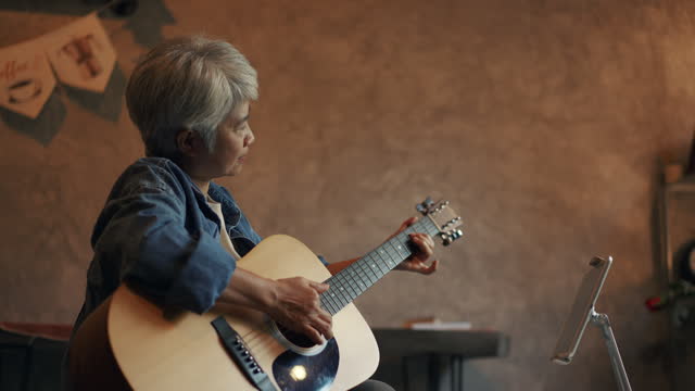 relaxed senior woman resting on comfortable plays guitar at home