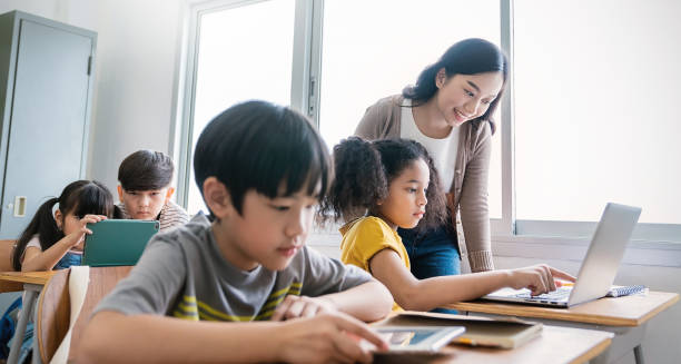 istock Pupil girl, teacher learn computer in classroom at elementary school. Student boy studying primary school. Children coding online in classroom. Education knowledge, successful teamwork concept banner 2147675308