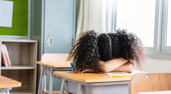 Portrait of little black pupil girl sleep take a nap in classroom at the elementary school. Student girl study doing test in primary school. Burnout overload tried in class. Education knowledge