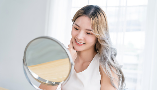 Closeup portrait young beautiful asian girl with mirror makeup routine with copy space. Beauty influencer woman perfect glow touch skin dress up. Healthcare woman lifestyle cosmetic blogger concept photo