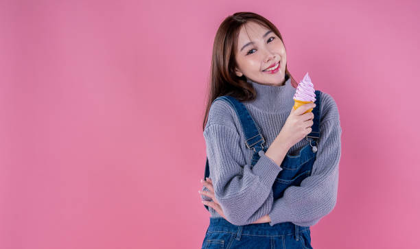 Portrait of happy korean model girl. Joyful adorable teenage girl smile broadly with eat tasty ice cream. Asian beauty woman has fun enjoys summer in stylish bib jeans clothes isolated on pink wall retrato de una chica modelo coreana feliz. la alegre y adorable adolescente sonríe ampliamente con un sabroso helado. la mujer de belleza asiática se divierte disfruta del verano con elegantes jeans con babero ropa aislada en la pared rosa
