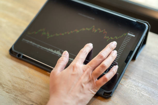 Action of an investor hand is touching on tablet displat to review the stock investment value graph. Business investment scene photo, close-up and selective focus.
