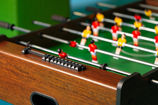 A detailed view of a foosball table featuring miniature players in red and blue colors competing in a fast-paced game. The figures are strategically positioned on metal rods, aiming to score goals by moving back and forth across the table.