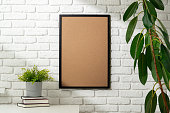 Blank Photo Frame on White Brick Wall With Houseplants and Books