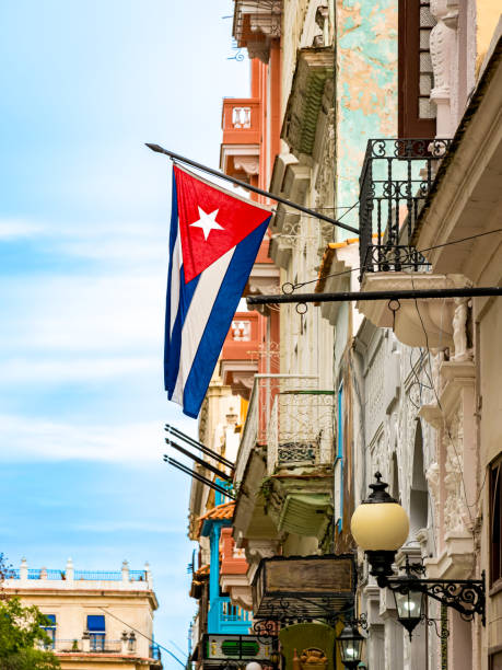 A portrait low-angle view captures the Cuban flag hanging down from an old colonial-style house facade in Havana Old Town, a patriotic symbol with ample copy space, ideal for travel-themed designs.