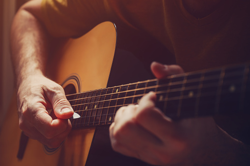 Man playing acoustic guitar at home, low key image with selective focus