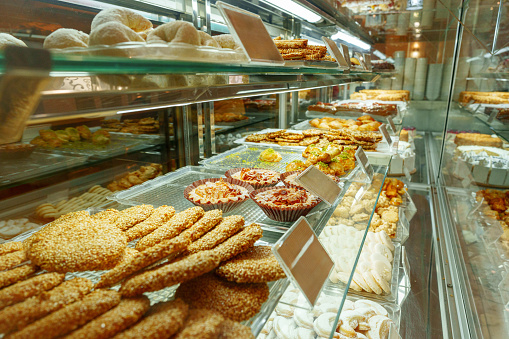 An array of freshly baked pastries and sweets temptingly showcased behind the glass display of a bakery shop. The selection includes cookies, cakes, and other confections that promise a treat for the taste buds.